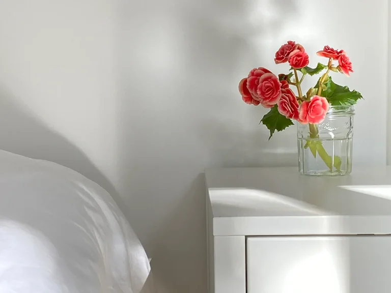 red and orange flowers in a white vase by a bed