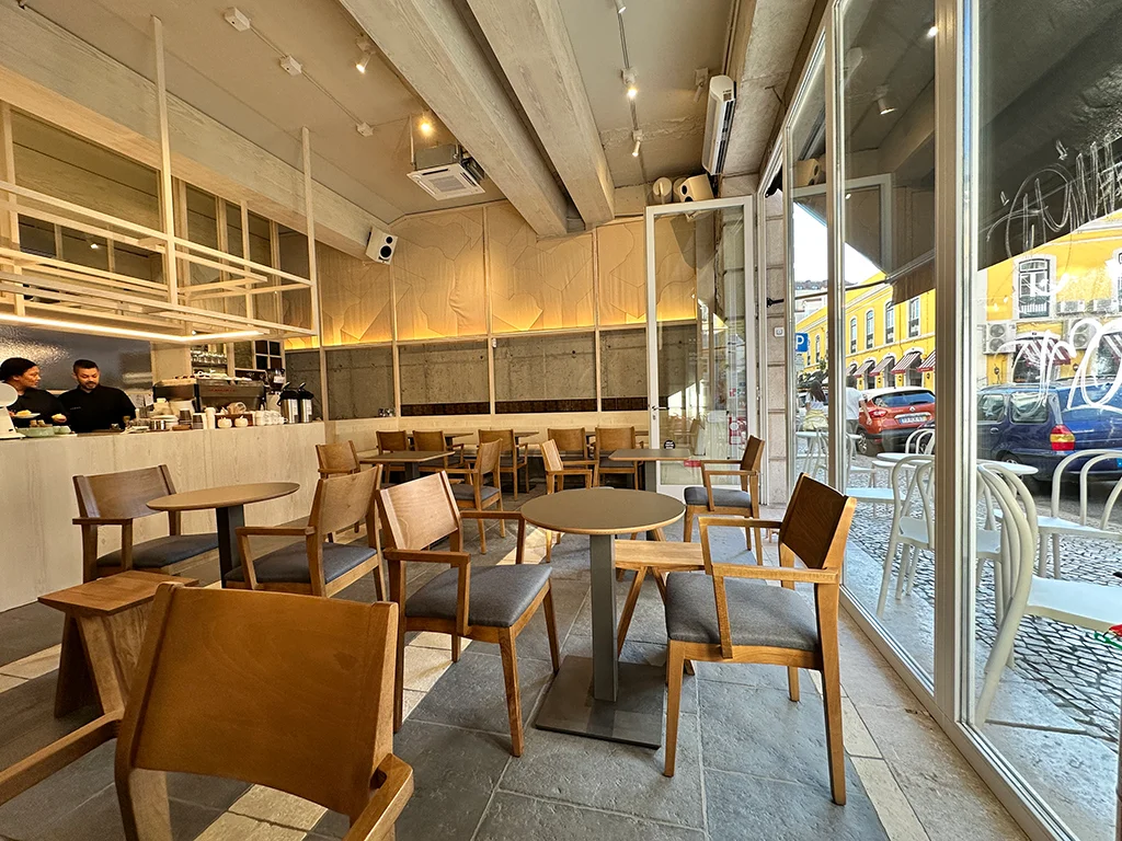 Interior of restaurant, light wood chairs, dark tables, steel, large windows, white and beige color theme