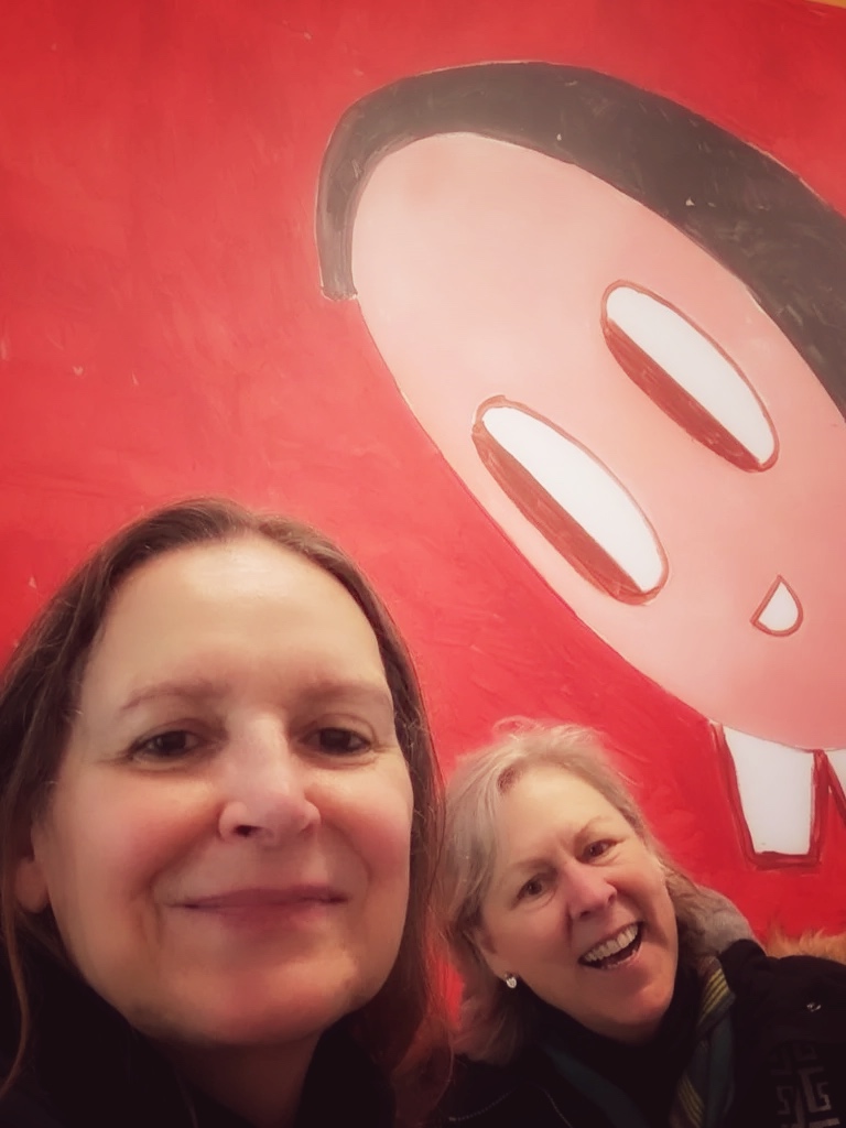 photo of Monica from London London and Marguerite 50 and Rising, in front of poster, red background at Saatchi Gallery