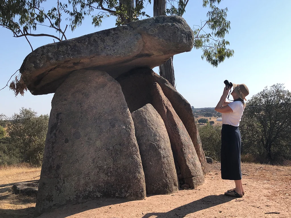 woman wearing a skirt , hat, photographing a megalith stone in the Alentejo